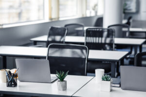 Modern office building interior and coronacrisis during quarantine. Focus on worker desk, chair, laptop and plants in room with columns and large windows in daylight, flat lay, free space