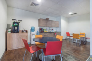 A room in a modern office for relaxing and snacking. A small kitchen set, a cooler and
a coffee machine. Round tables and colorful chairs.